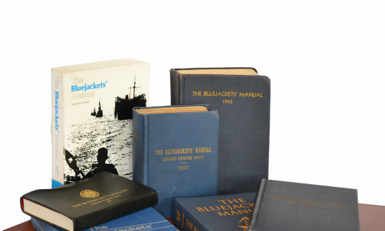 Seven different editions of the Bluejacket's Manual on a table